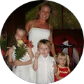 Jennifer Lowrey Woman standing behind three young children, all dressed up, with one girl holding a bouquet of flowers.