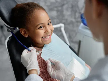 about-image-3 Smiling child sitting in dental chair, interacting with dentist during checkup.