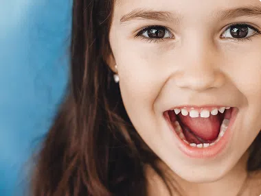 image-1 Young girl smiling with mouth open, showing clean teeth for pediatric dental care.