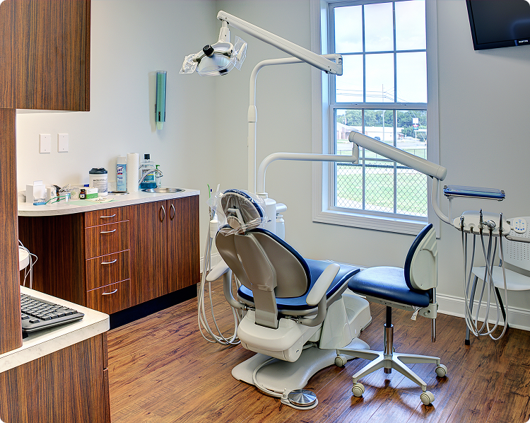 Modern dental exam room with patient chair, overhead light, and clean countertop with dental supplies.