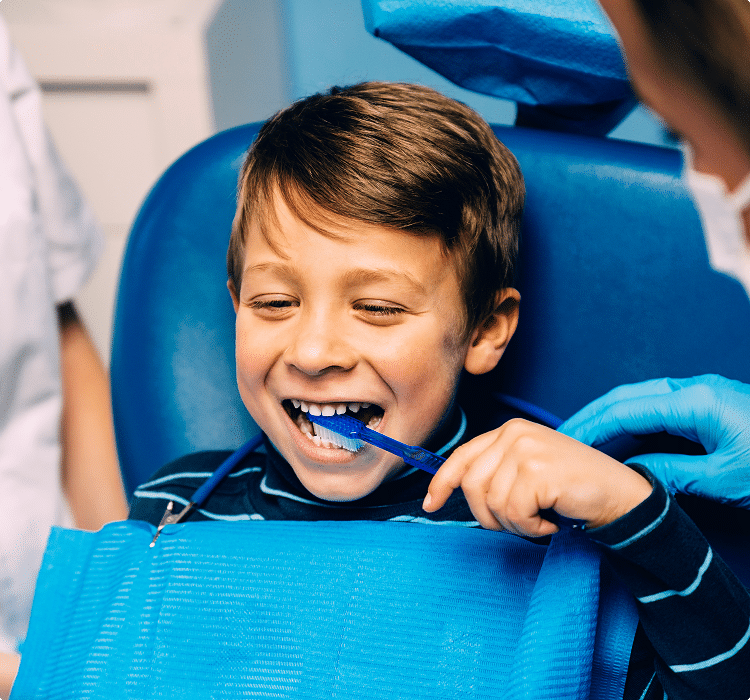Smiling boy in dental chair learning to brush teeth during a dental hygiene lesson.