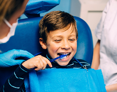 Smiling boy brushing his teeth during a dental visit, guided by dental professionals.