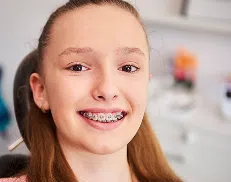 service-image (9) Smiling girl with braces sitting in a dental chair during an orthodontic appointment.