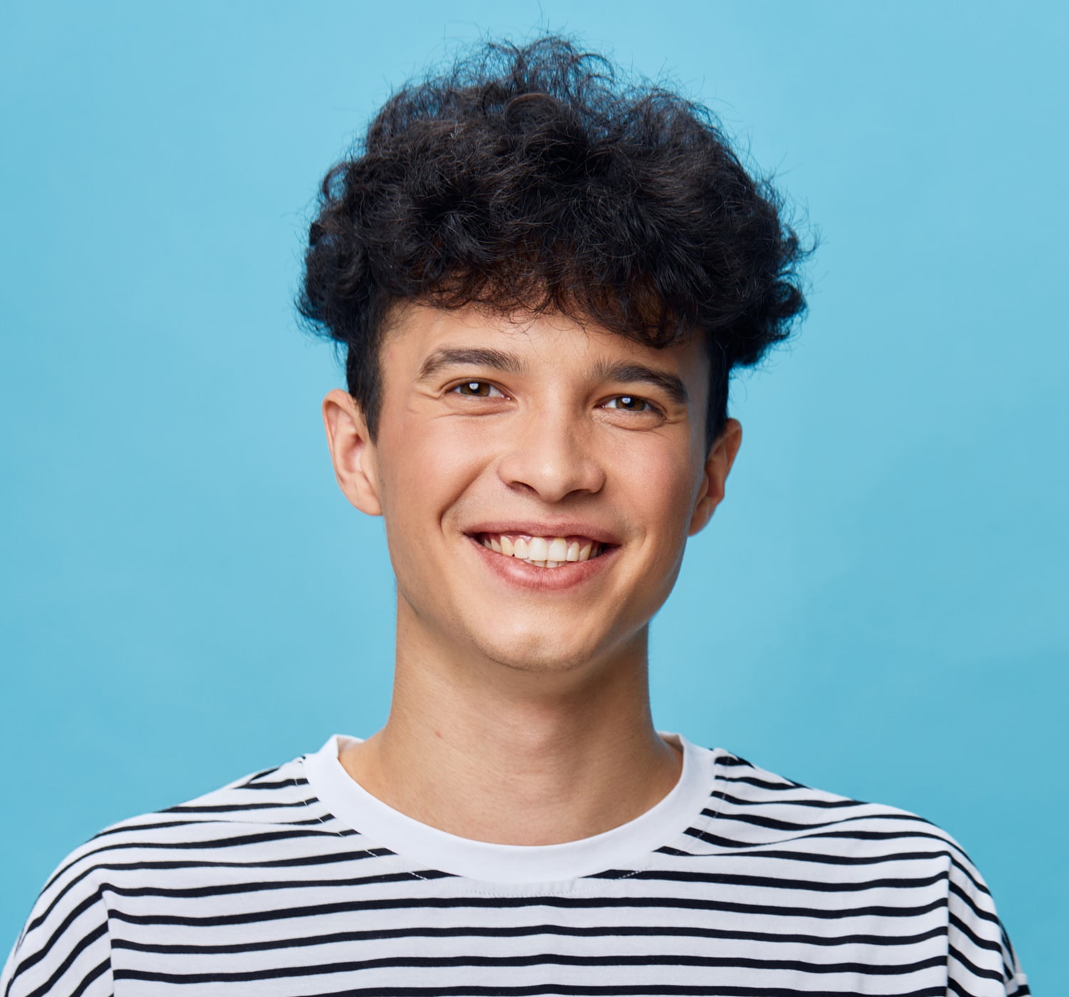 FSC-generaluse-image11-min Young man smiling in front of a blue background, wearing a black and white striped shirt.