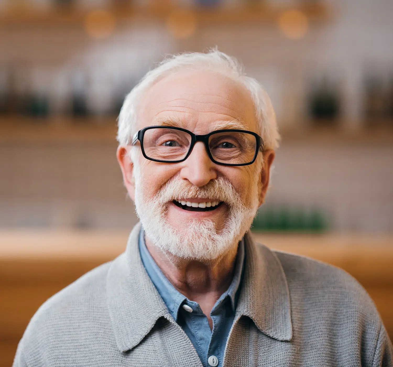 Smiling elderly man with white hair and glasses, wearing a grey sweater.