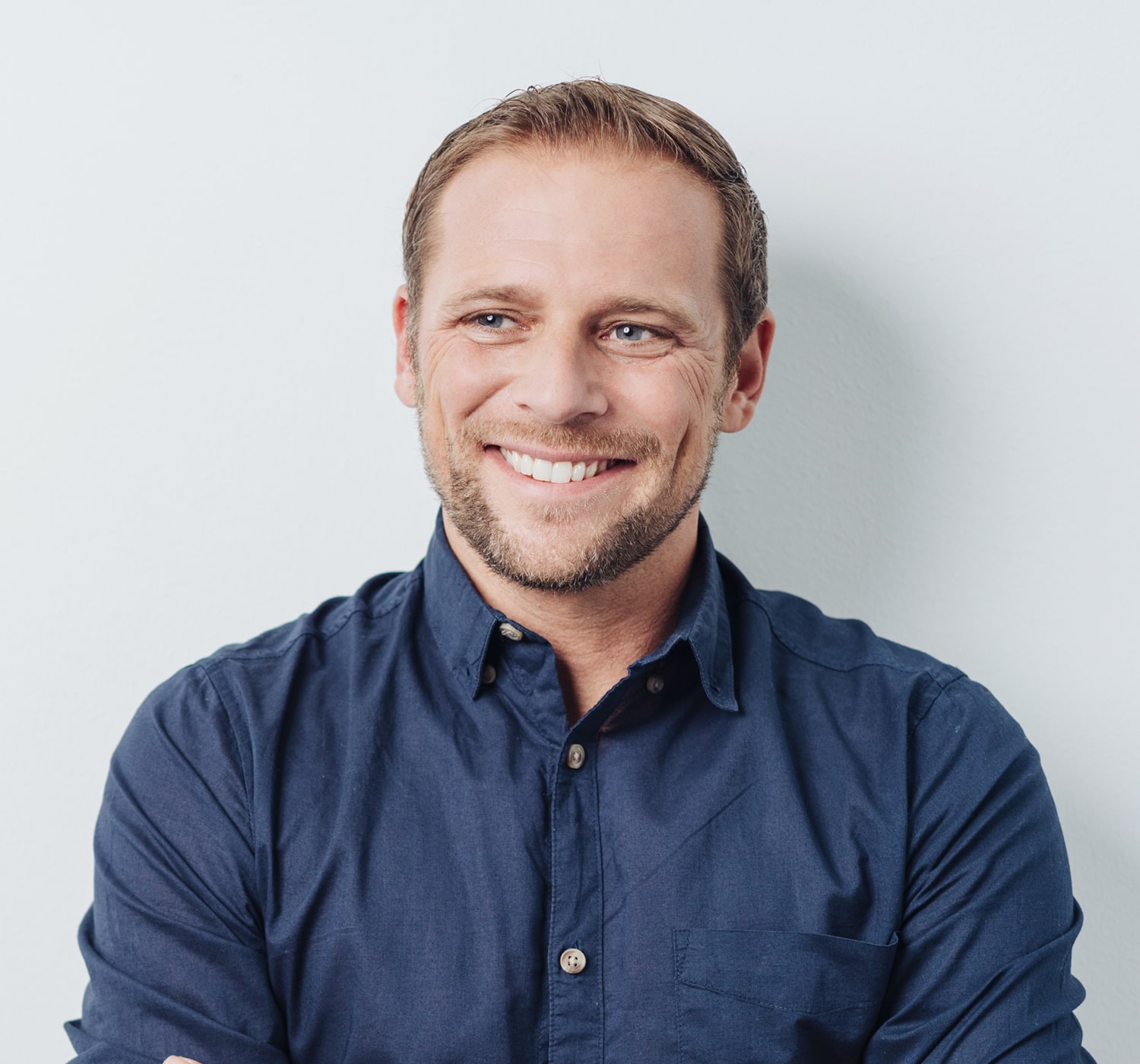 FSC-generaluse-image5-min Smiling man in a navy blue shirt looking to the side, standing against a plain light background.