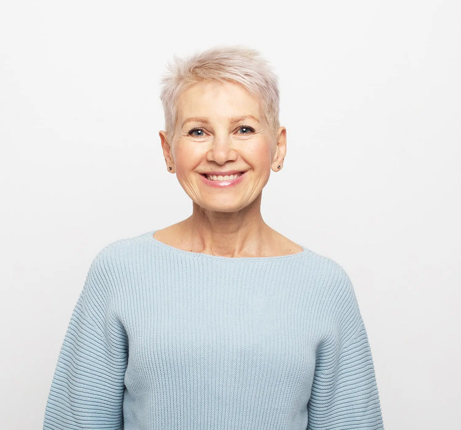 Smiling older woman in a light blue sweater posing against a plain white background.