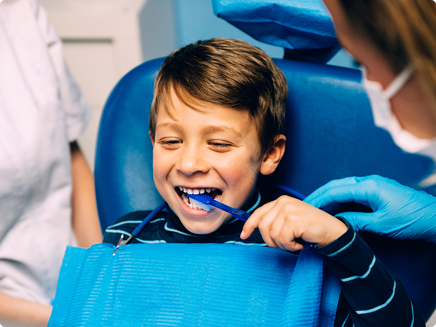 Smiling boy in dental chair learning to brush teeth during a dental hygiene lesson.
