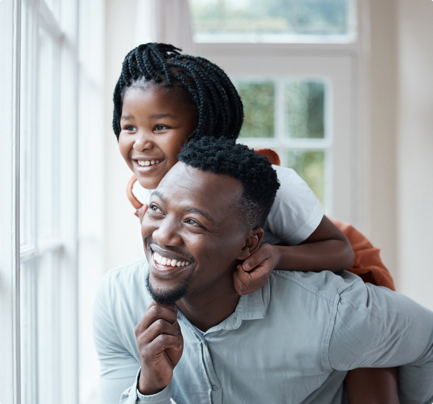 fsc-general-image (1)-min Smiling father giving daughter a piggyback ride as they look out a window, capturing a joyful family moment.