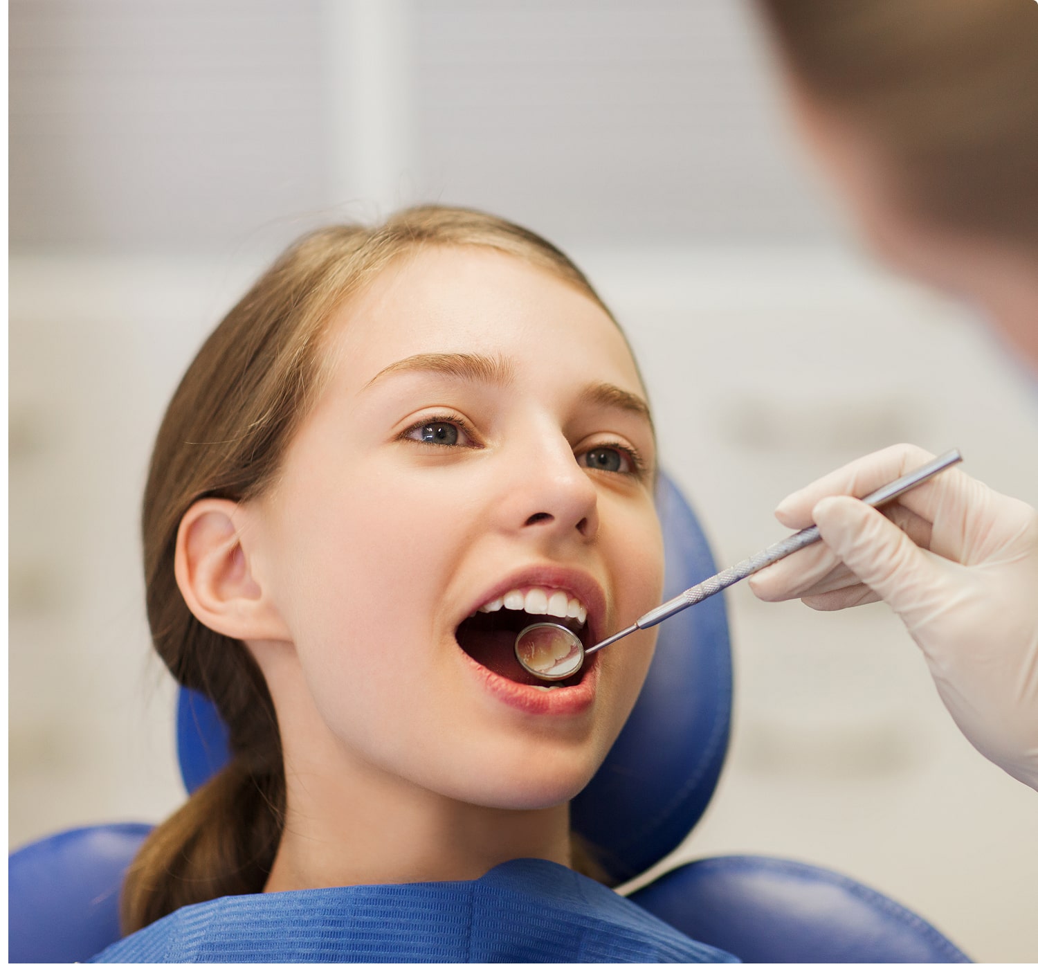 Teen girl getting a dental checkup, with a mirror tool examining her teeth for oral health.