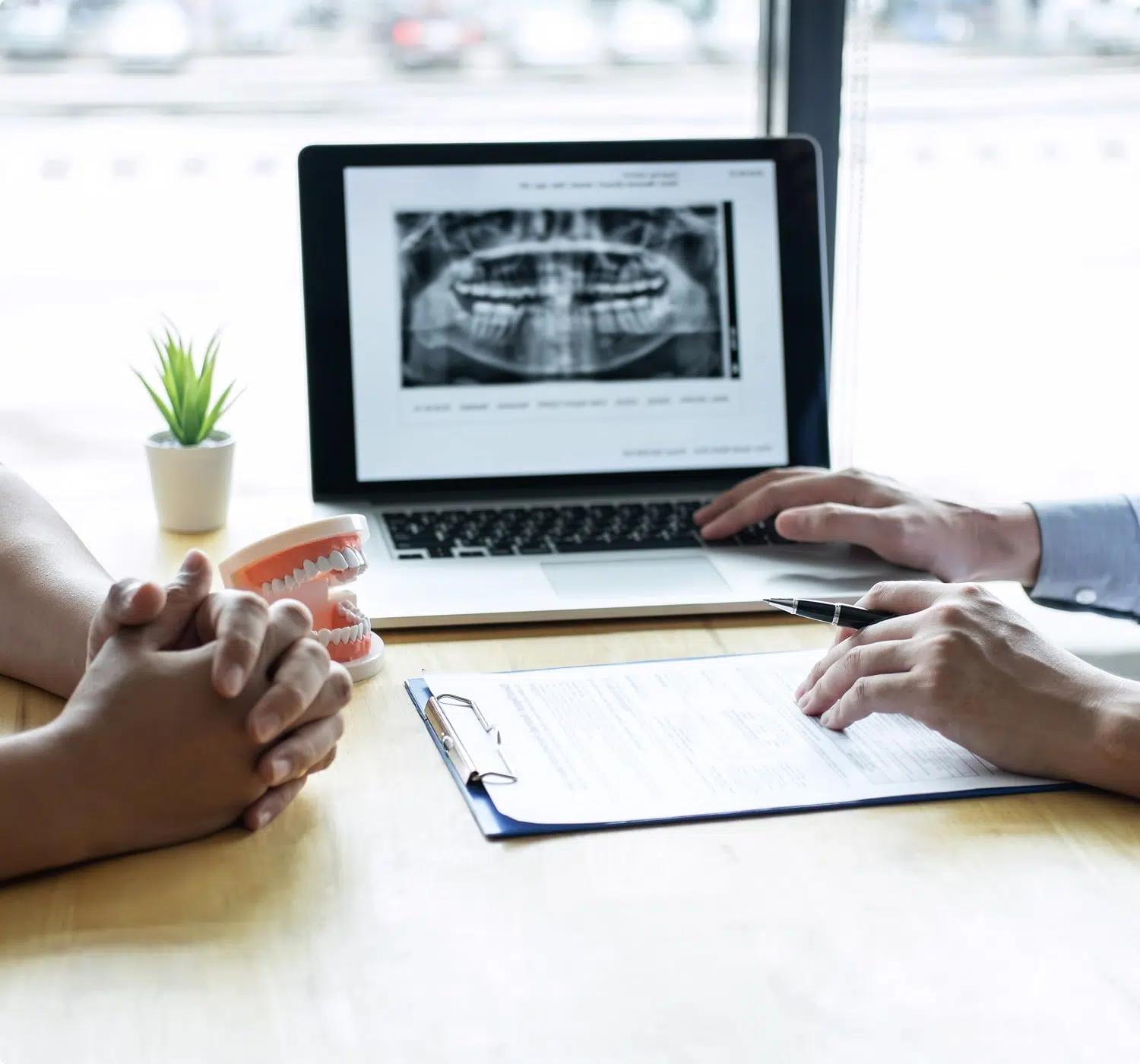 Dentist discussing dental X-ray and treatment plan with patient at consultation table.