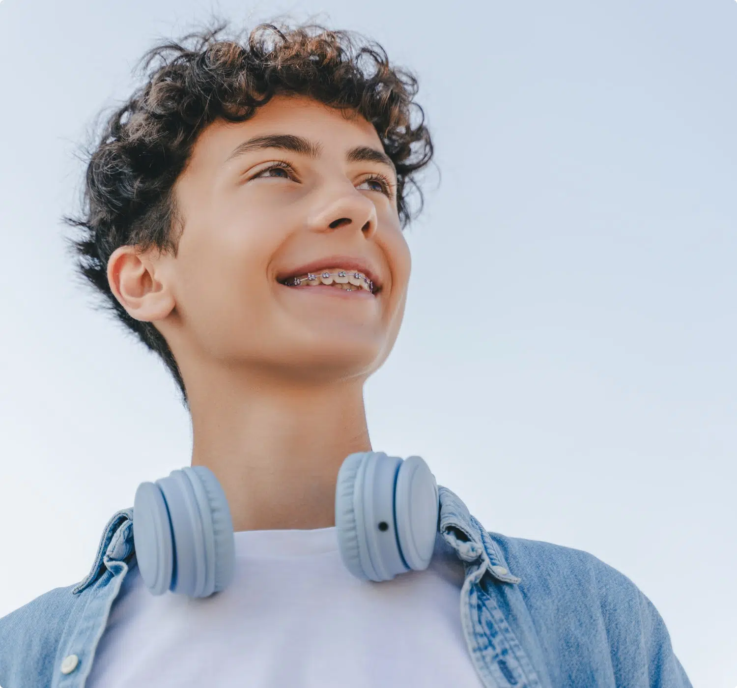 fsc-general-image (17)-min Smiling teen with braces looks up confidently, wearing headphones around neck and a denim shirt.