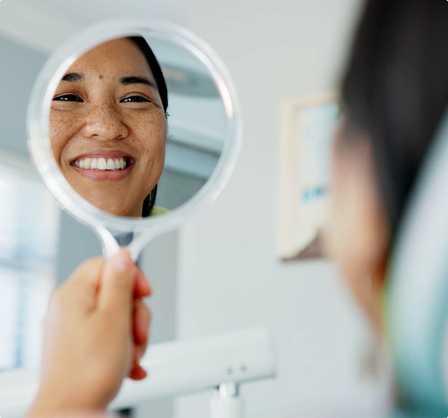 fsc-general-image (6)-min Person smiling while examining their teeth in a handheld mirror after dental treatment.