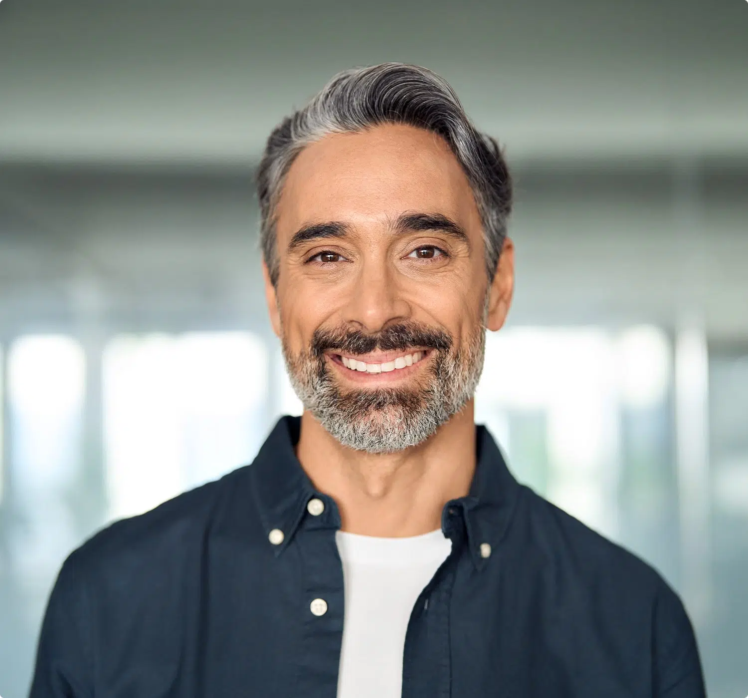 Smiling man with salt-and-pepper hair posing confidently in a brightly lit office setting.