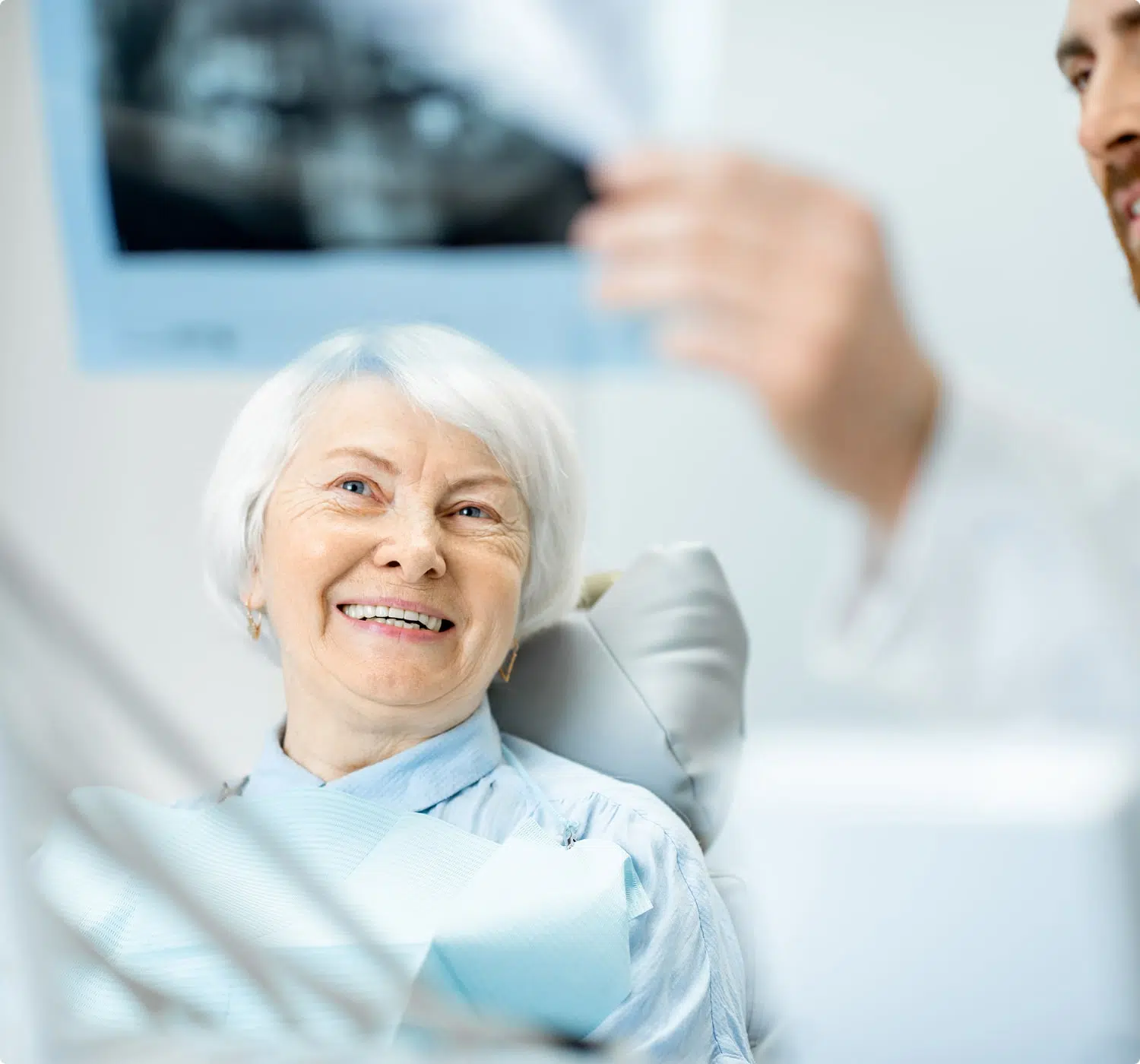 Smiling older woman in a dental chair listening as a dentist reviews her X-ray.