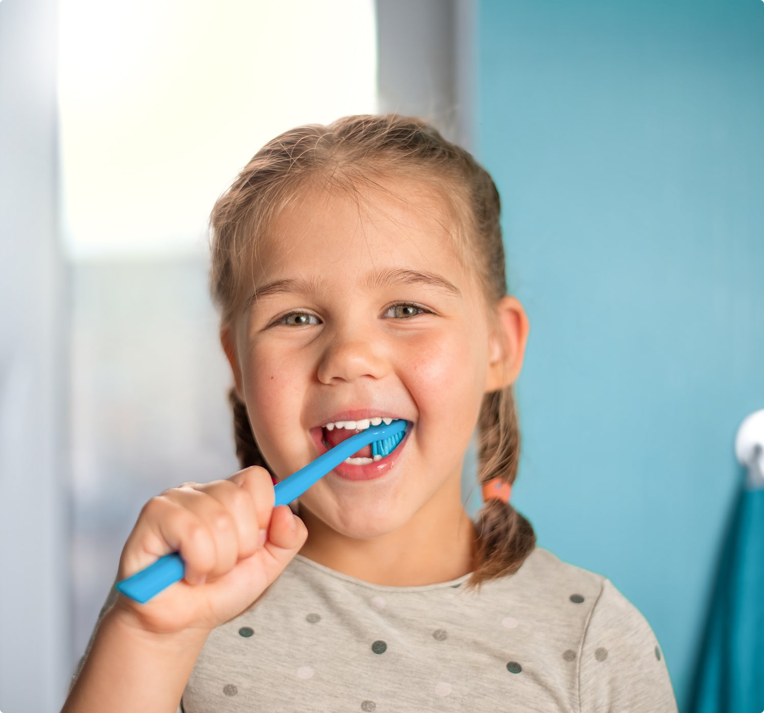 fsc-general-image-min Young girl smiling while brushing her teeth with a blue toothbrush, promoting good dental hygiene.