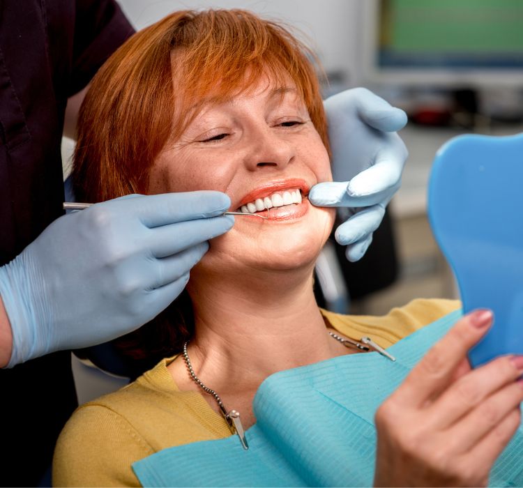 Middle-aged woman with red hair looking at smile in mirror during dental appointment