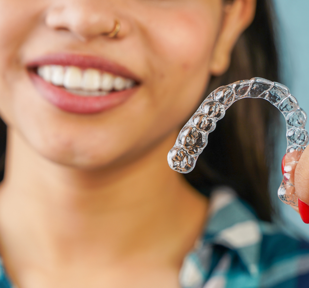 A woman smiling holding Invisalign tray.