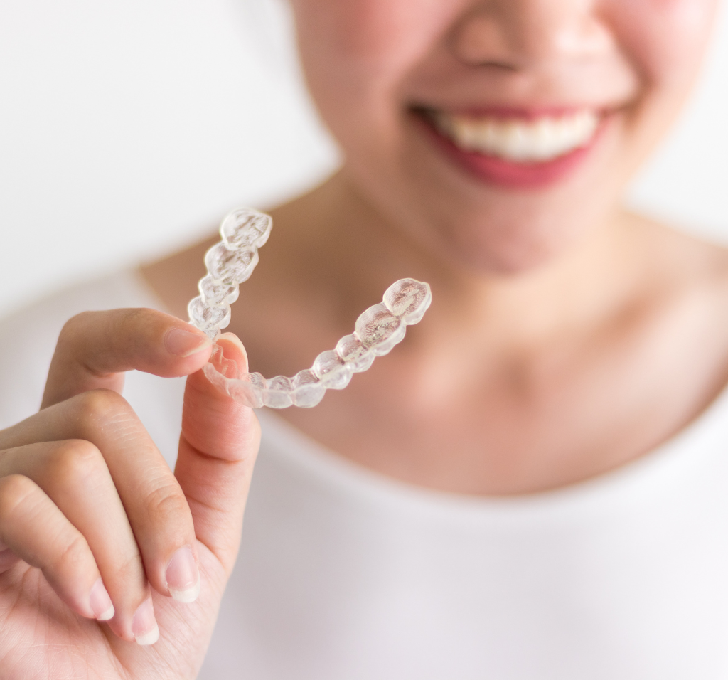 A woman smiling with straight teeth holding a clear aligner.