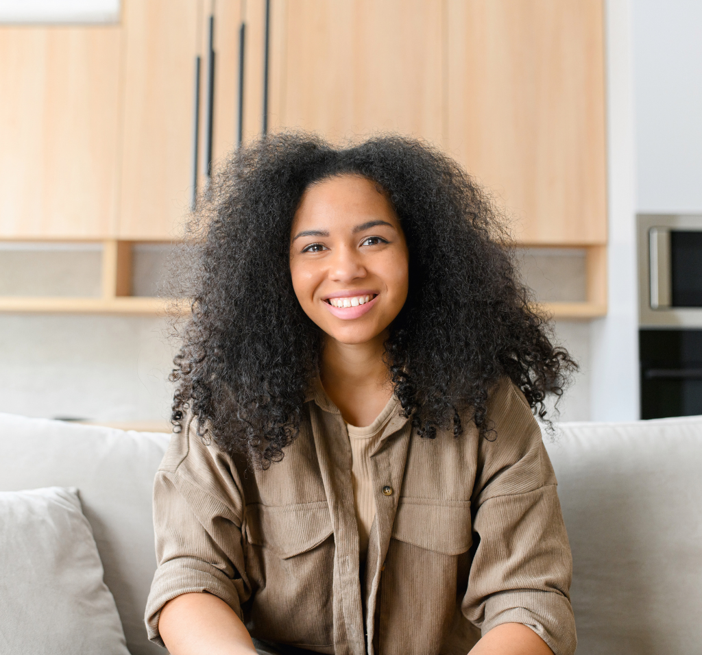 A woman with curly brunette hair sitting on couch smiling