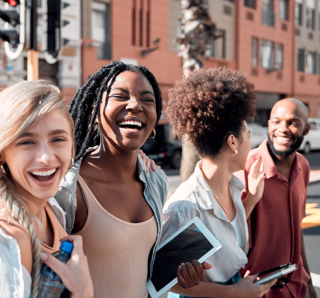 Four young adults 3 women and one man smiling while walking downtown.